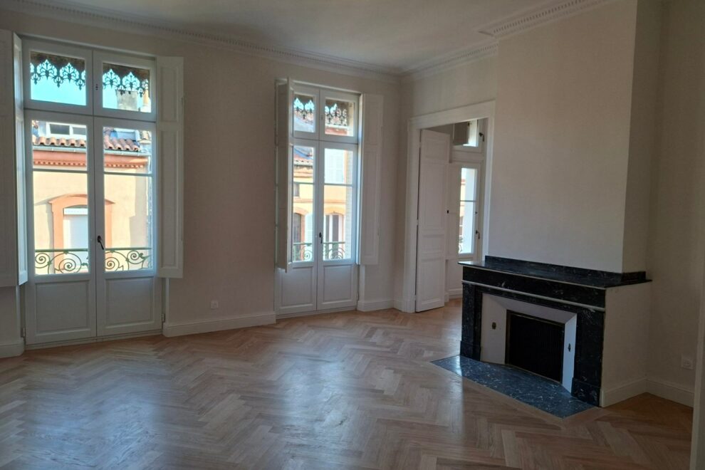 Salon d'un appartement ancien rénové : corniches moulurées, cheminée en marbre noir et portes-fenêtres