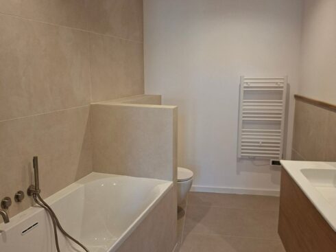 Salle de bain avec baignoire, murs blancs et grands carreaux beiges