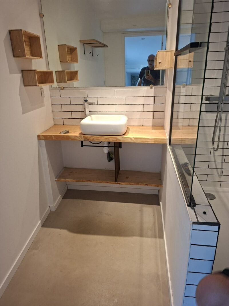 Meuble vasque en bois et étagères murales dans la salle de bain rénovée