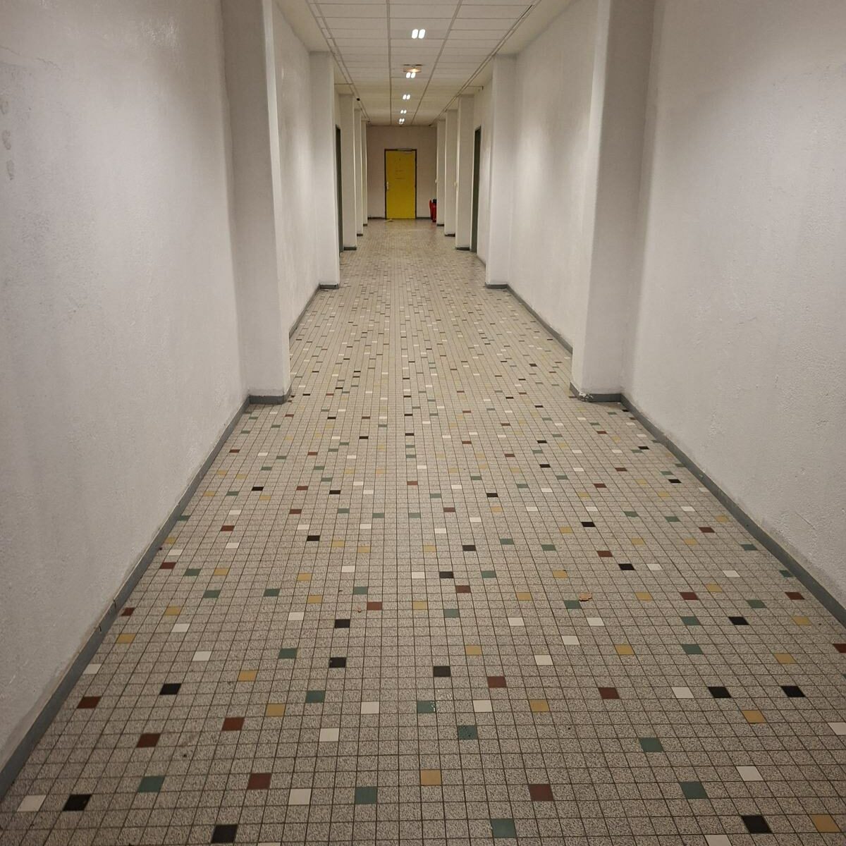 Rénovation de couloirs à Pamiers : long couloir blanc, portes colorées et sol en mosaïque