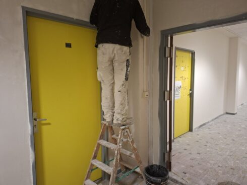 Peintre d'AB Peinture sur escabeau, reprise des murs près d'une porte jaune