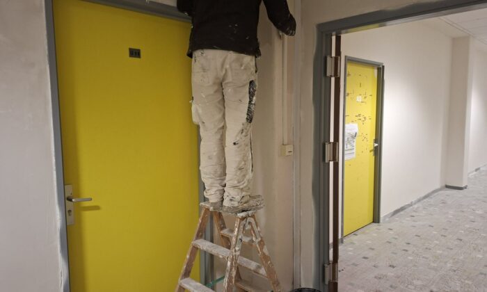 Peintre d'AB Peinture sur escabeau, reprise des murs près d'une porte jaune